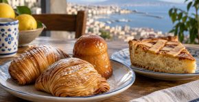 Pasteles de masa laminada, un babà brillante y una porción de pastiera con enrejado, con la bahía de Nápoles al fondo.